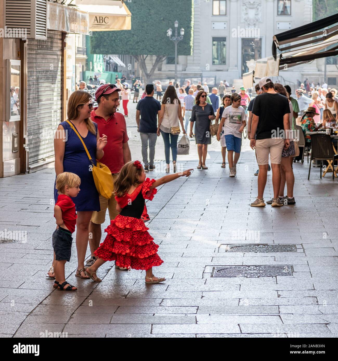 Ein junges Mädchen in einem roten Flamenco-Kleid zeigt aufgeregt auf etwas in einem Schaufenster in der Calle Sierpes, Sevilla Stockfoto