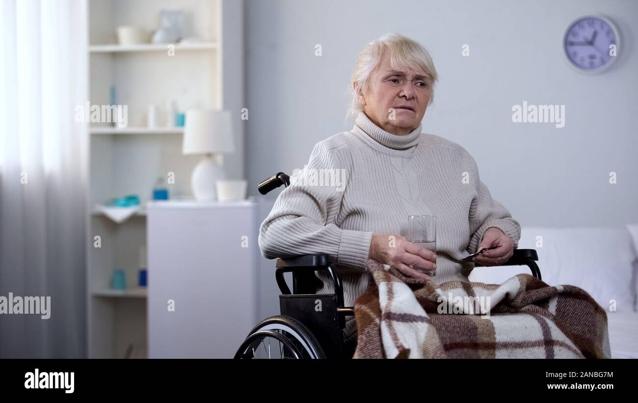 Reife Lady im Rollstuhl leiden unter Schmerzen halten Medikamente, Pflegeheim Stockfoto