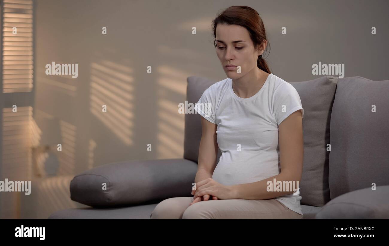 Schwangere Frau sitzt auf einem Sofa gedrückt, unerwünschte Schwangerschaft, Leben Schwierigkeiten Stockfoto