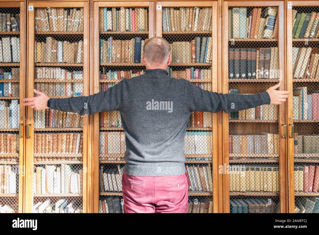 Mann, der versucht, das Wissen aus den Büchern auf den Bücherregalen zu ergreifen Stockfoto