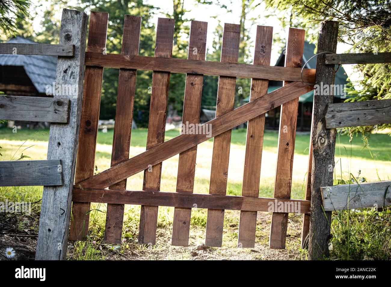 Alte Braune hölzerne Tor und Zaun um einen grünen Garten Stockfoto
