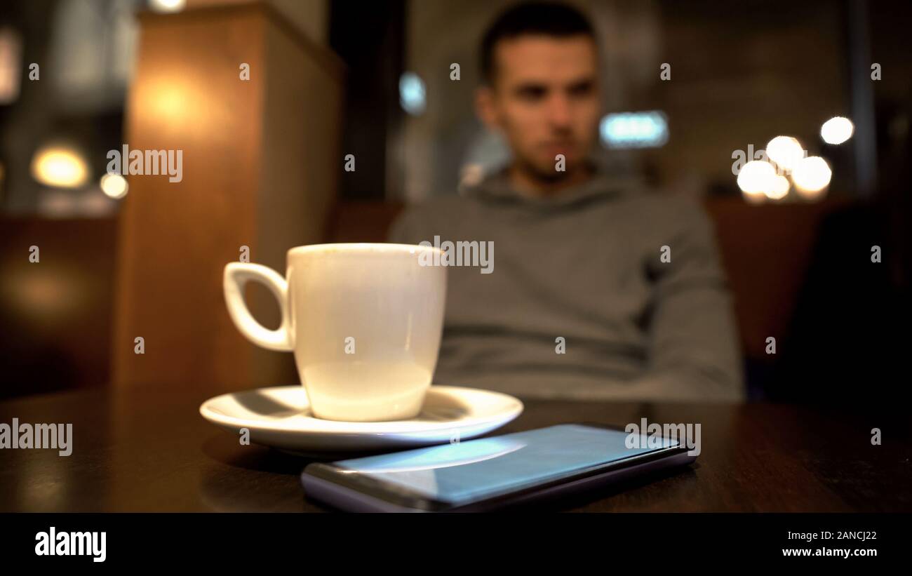 Einsamer Mann im Cafe sitzen, Telefon liegen auf dem Tisch und wartet darauf, dass Frau auf Datum Stockfoto