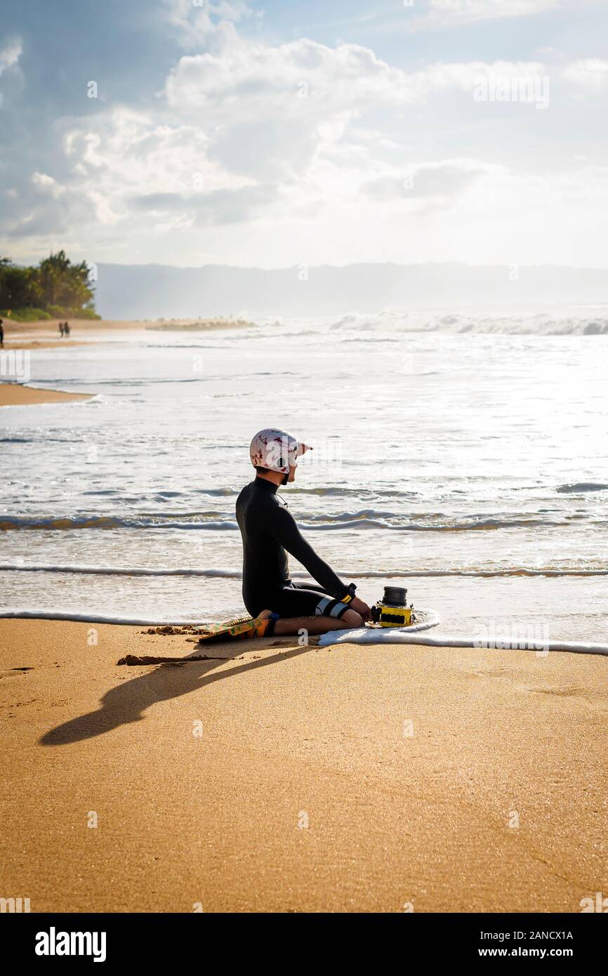 Ein Surf-Fotograf sitzt auf dem Sand und schaut auf das Meer Stockfoto