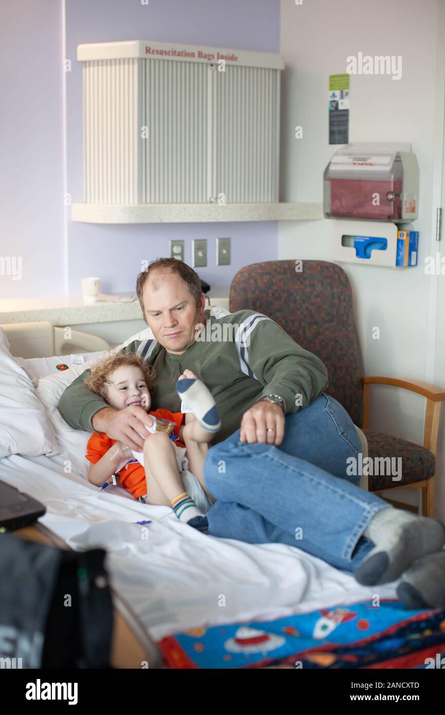 Besorgte Vater kuschelt mit dummen Kleinkind im Krankenhausbett. Stockfoto