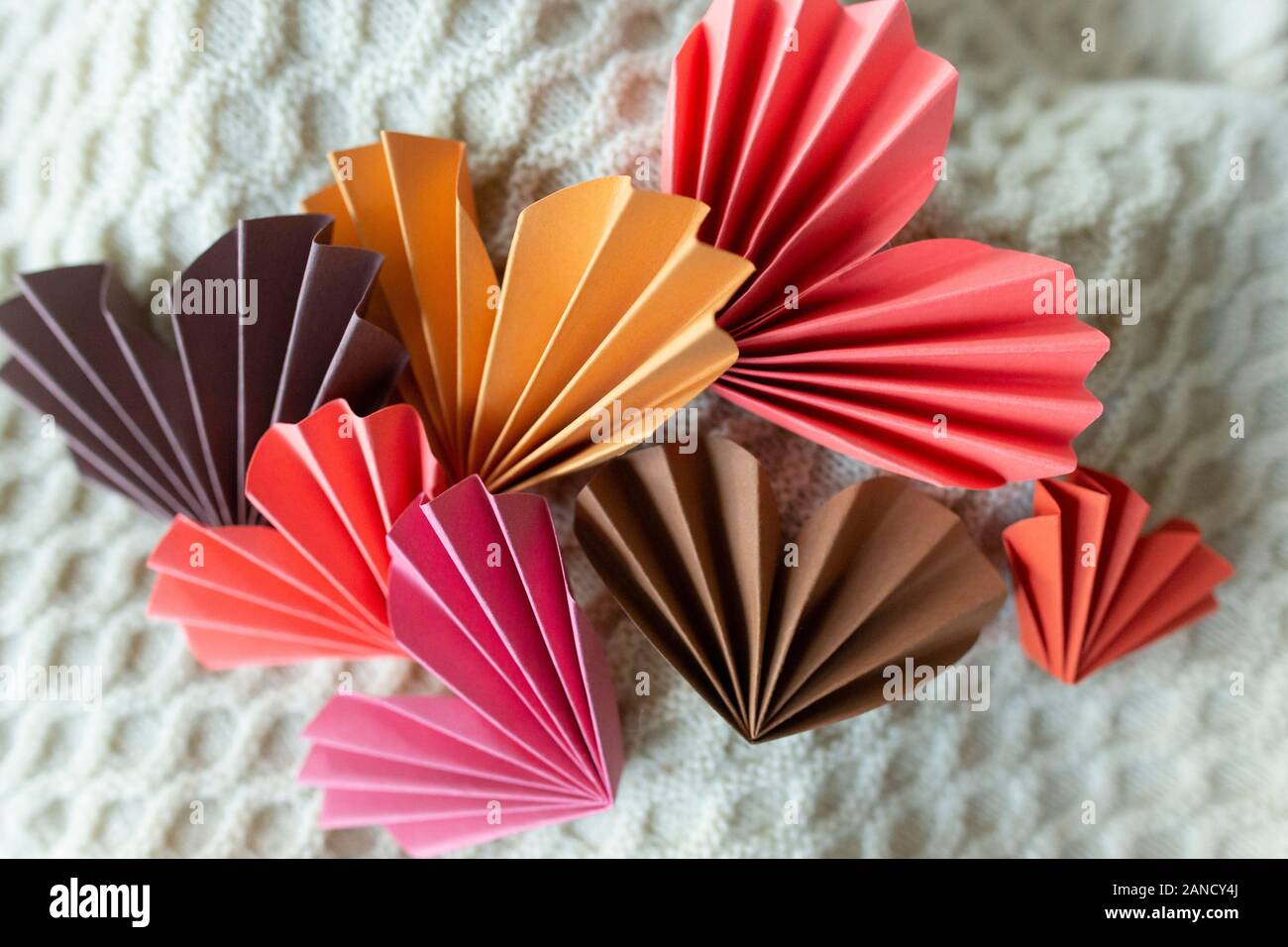 Mehrfarbige Origami-Papier Herzen vor gestricktem Hintergrund Stockfoto