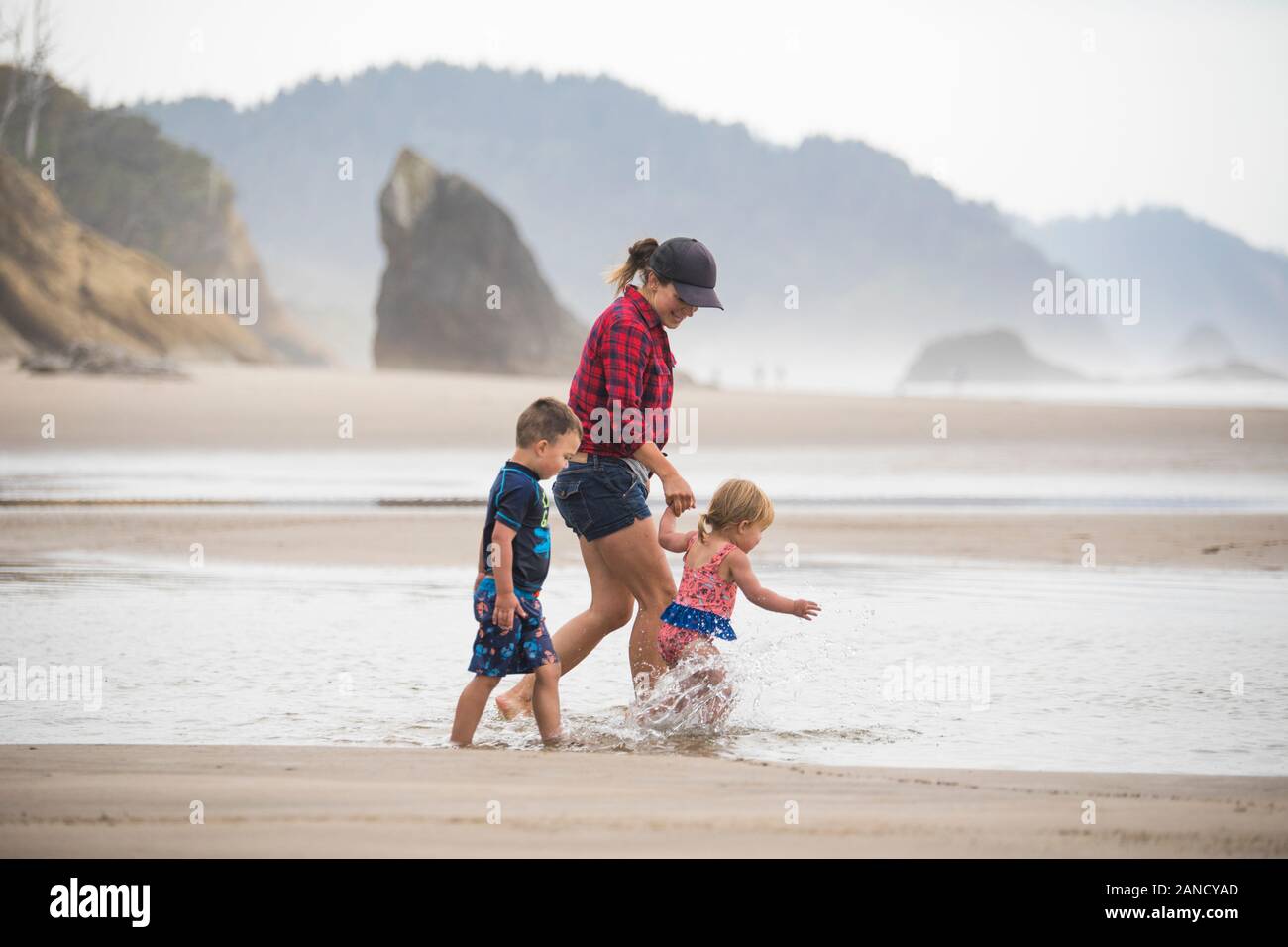 Seitenansicht der Mutter, die mit ihren beiden kleinen Kindern am Strand spazieren ging. Stockfoto
