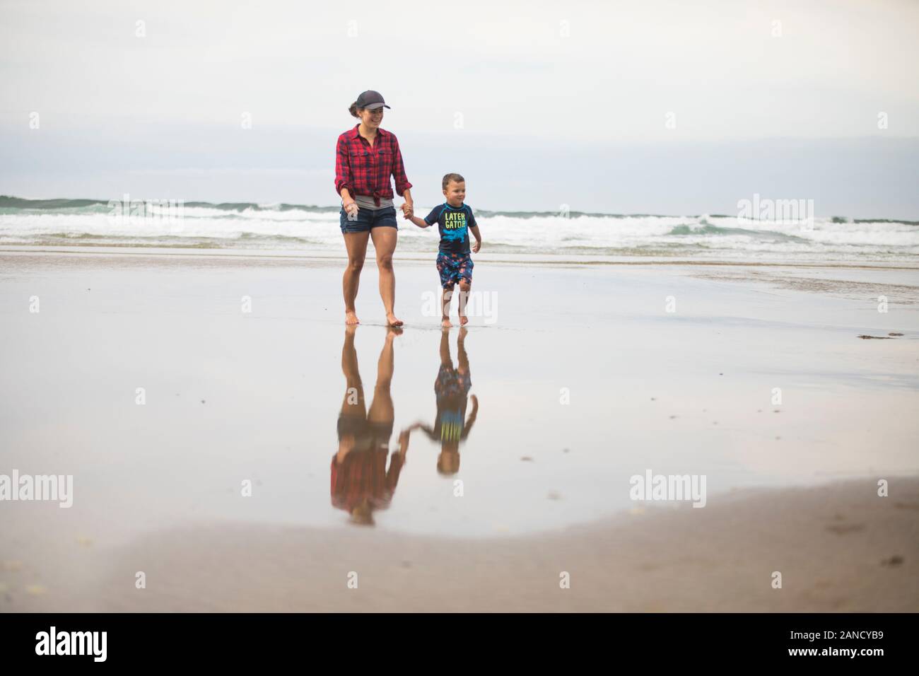 Mutter, die am Strand geht, hält die Hände mit ihrem Sohn. Stockfoto