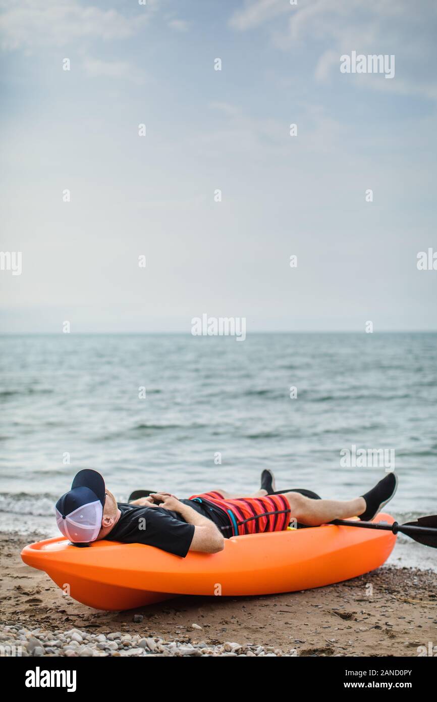 Mann, der während der Sommerferien ein Nickerchen auf dem Kajak am Strand macht Stockfoto