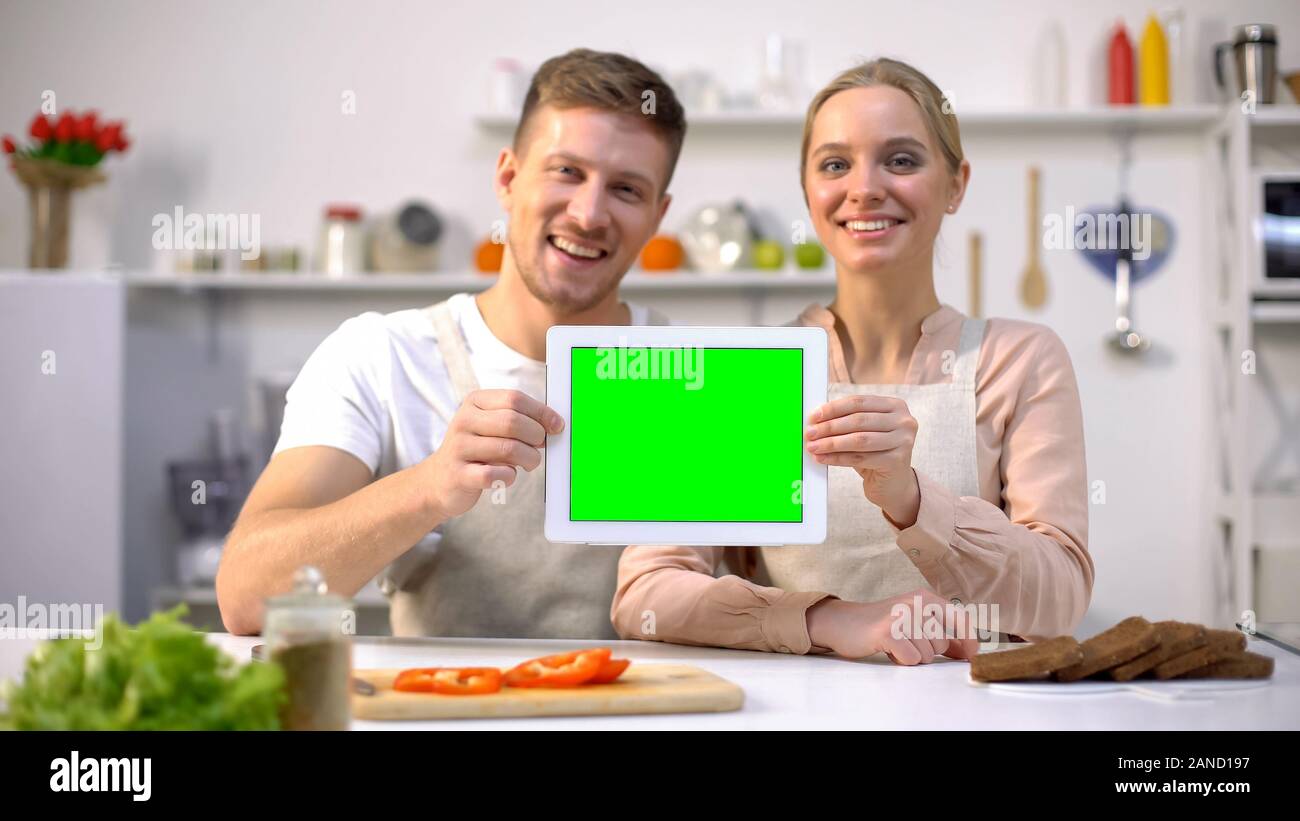 Junge lächelnde Paar zeigen Tablet mit Green Screen, kulinarische Kurse Vorlage Stockfoto