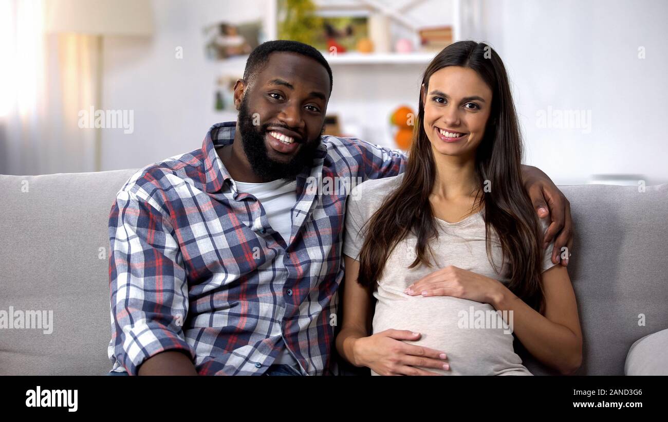Multiethnischen Paar in die Kamera schaut, schwangere Bauch Holding, IVF-Klinik Stockfoto