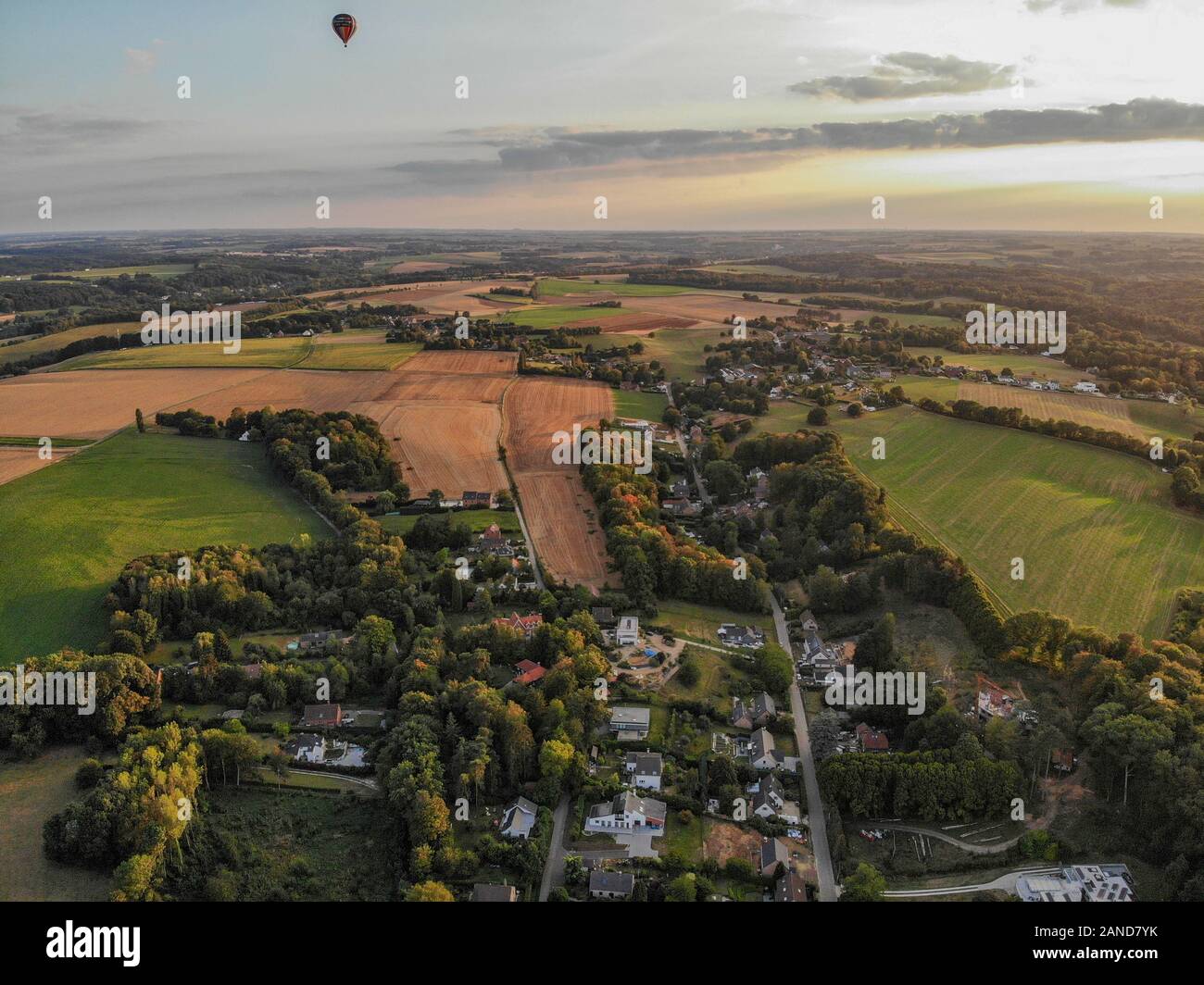 Heißluftballons am Himmel über schöne Ackerland Landschaft vor Sonnenuntergang. Bunte Heißluftballone fliegen über das Tal bei Sonnenuntergang. Belgien Stockfoto