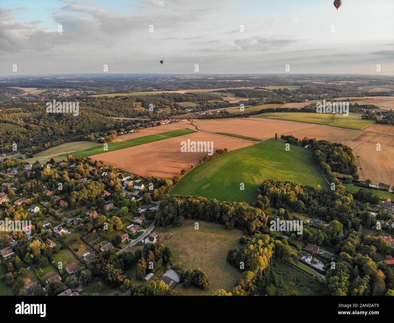 Heißluftballons am Himmel über schöne Ackerland Landschaft vor Sonnenuntergang. Bunte Heißluftballone fliegen über das Tal bei Sonnenuntergang. Belgien Stockfoto