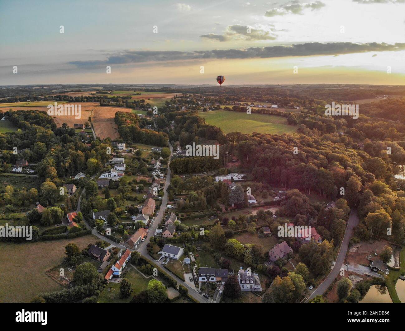 Heißluftballons am Himmel über schöne Ackerland Landschaft vor Sonnenuntergang. Bunte Heißluftballone fliegen über das Tal bei Sonnenuntergang. Belgien Stockfoto