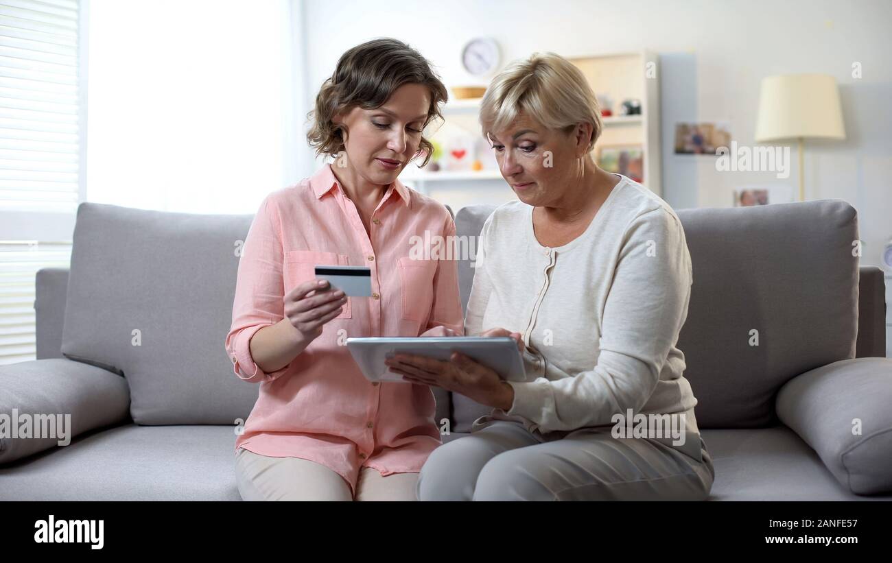 Tochter Lehre reife Mutter mit Tablette, die Eingabe der Kartennummer, online banking Stockfoto