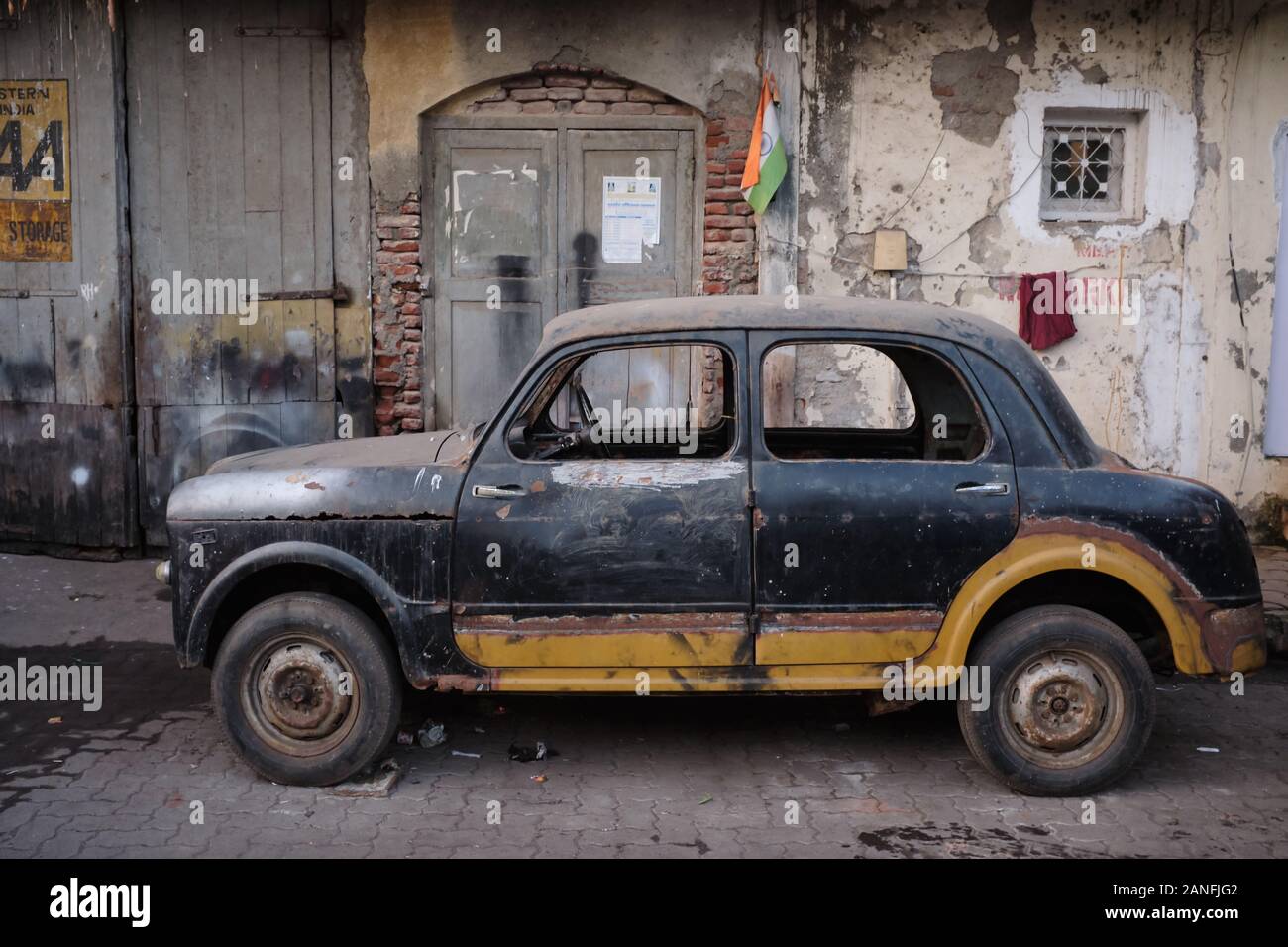 Ein verlassener, zerstörter alter Wagen, der in einer Gasse in der Nähe von Sassoon Docks in Colaba, Mumbai, Indien, steht Stockfoto