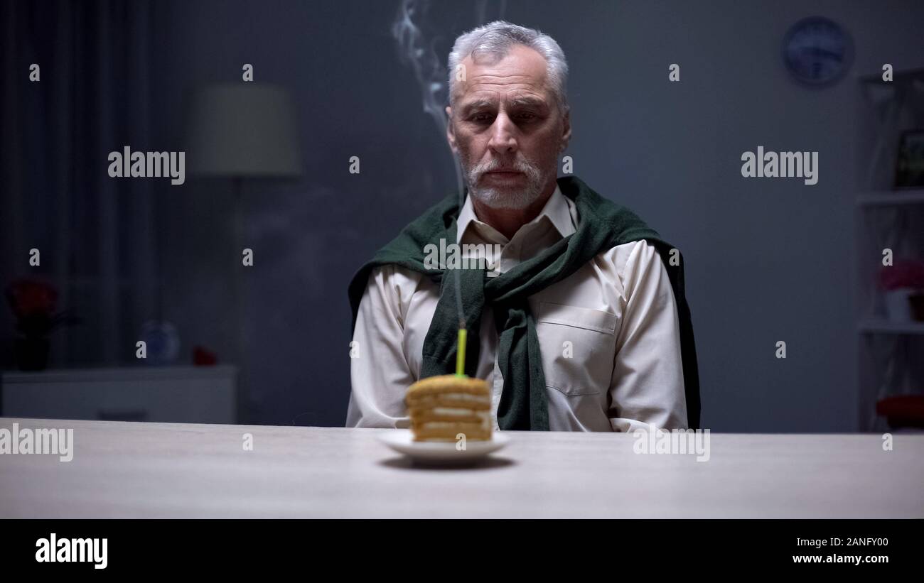 Unglücklich älterer Mann am Kuchen suchen und geblasen Kerze, trauriger Geburtstag, Einsamkeit Stockfoto