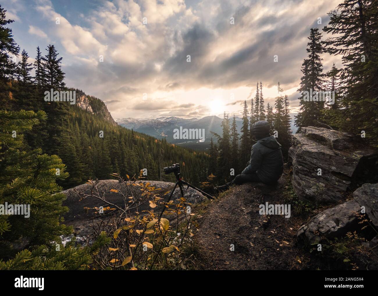 Mann Fotograf sitzen mit Besichtigung von Sunrise auf Klippe in Lake Louise, Banff National Park Stockfoto