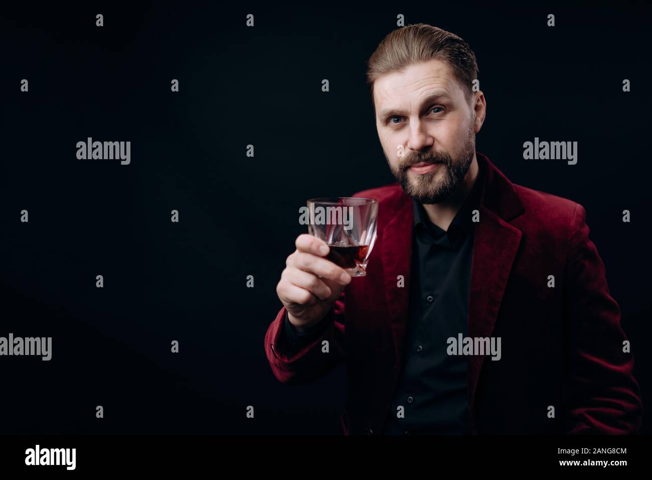 Stilvolle Mann in Weinigen Jacke Toasten mit einem Glas Spirituosen Stockfoto