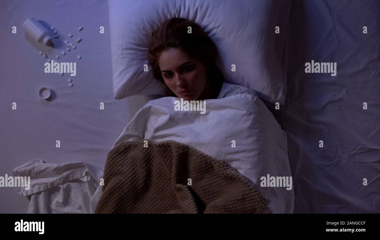Dame mit geöffneten Augen im Bett lag, in der Nähe von Glas mit Pillen, Selbstmordversuch, den Tod Stockfoto