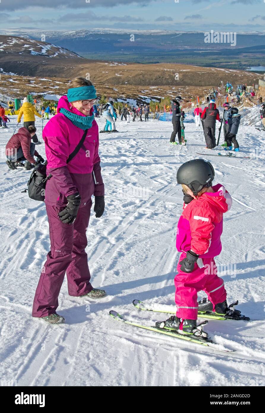 Fröhliche lächelnde Mutter, die kleine Mädchen auf Skiern betrachtet, Cairngorm Mountain Ski Center, Cairngorms National Park, Scottish Highlands, in der Nähe von Aviemore, Großbritannien Stockfoto