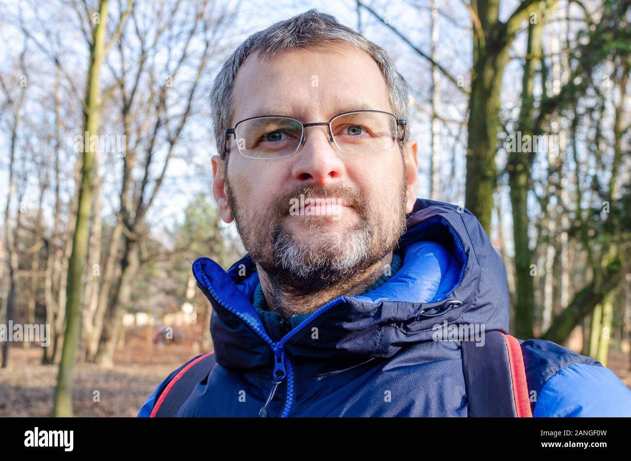 Porträt eines Mannes in einem Phantom blue Daunenjacke in den kargen Frühlingswald Stockfoto
