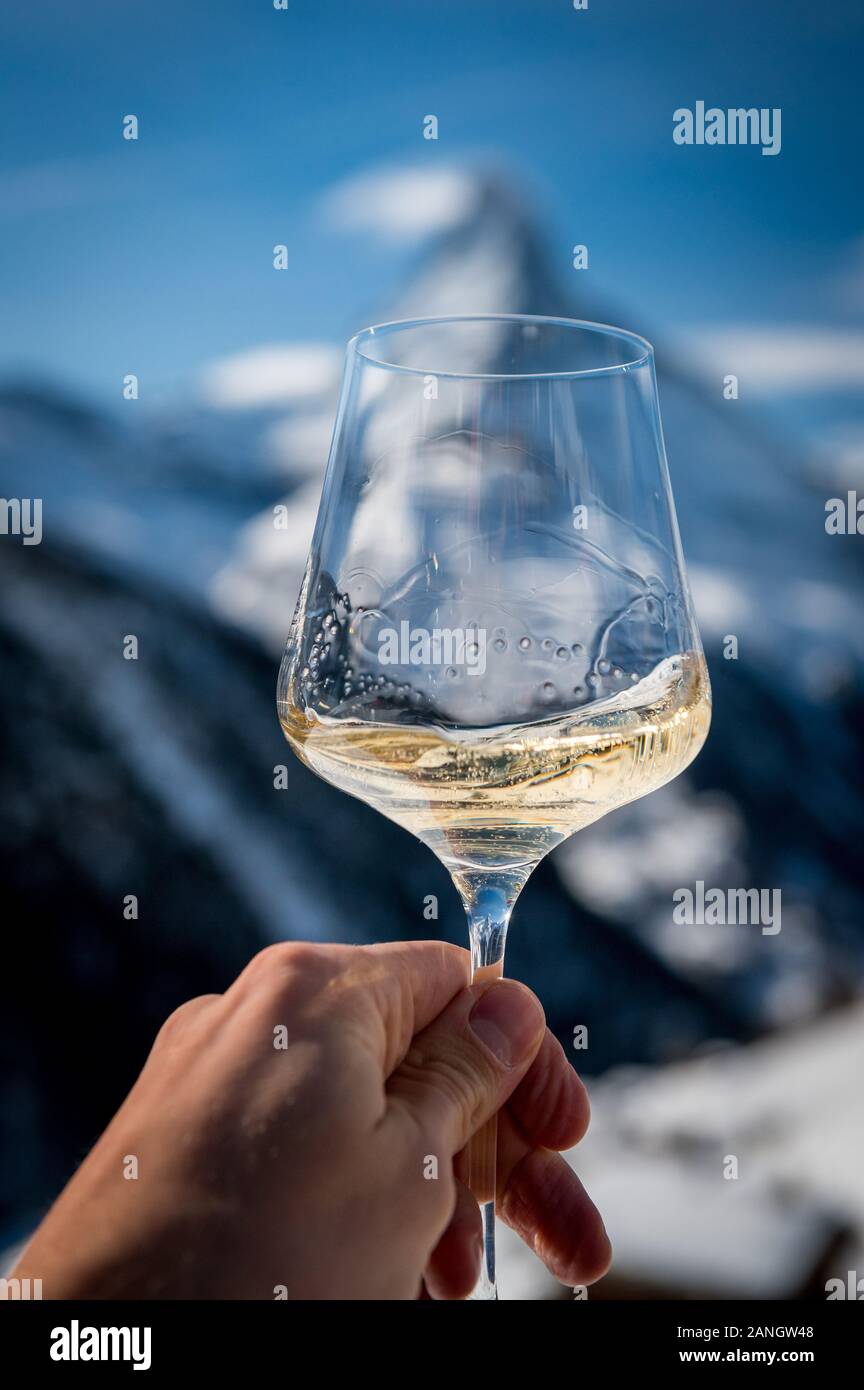 Hand mit einem Glas Weißwein vor Matterhorn im Winter in einem Restaurant Stockfoto