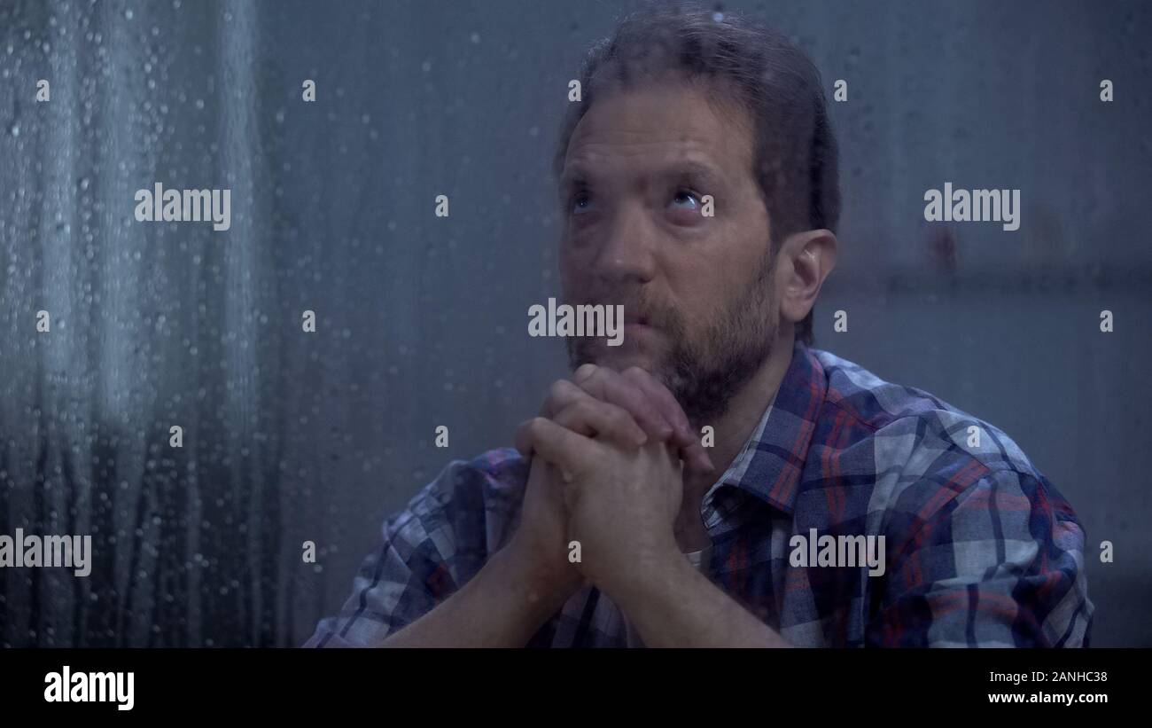 Hoffnungslosen männlichen Gott beten hinter regnerischen Fenster, um Hilfe zu bitten und Vergebung Stockfoto
