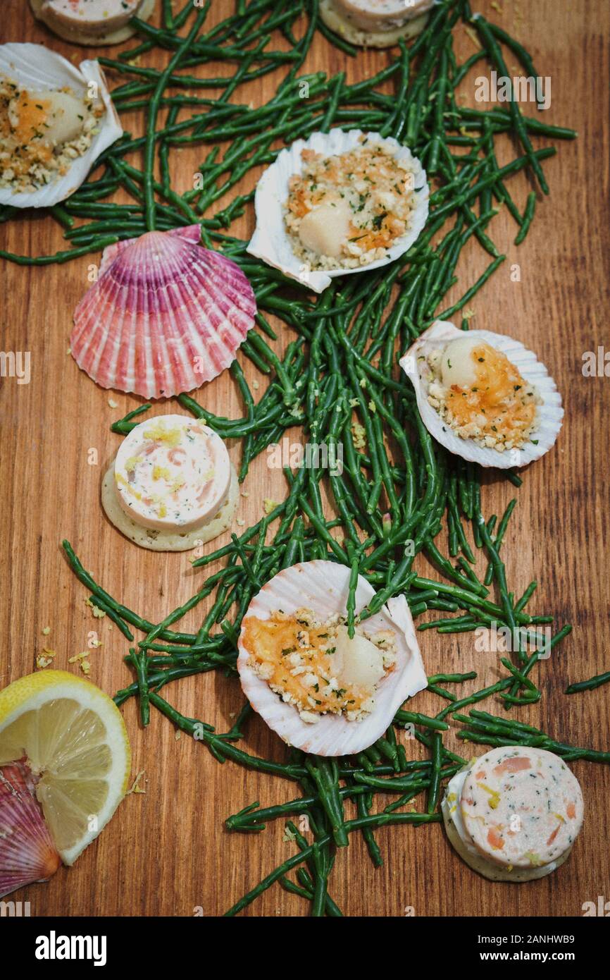 Meeresfrüchte-Platte: Kanapes auf Holzbrett mit Jakobsmuscheln und Samphire- und Zitronenkeilen. Draufsicht. Stockfoto