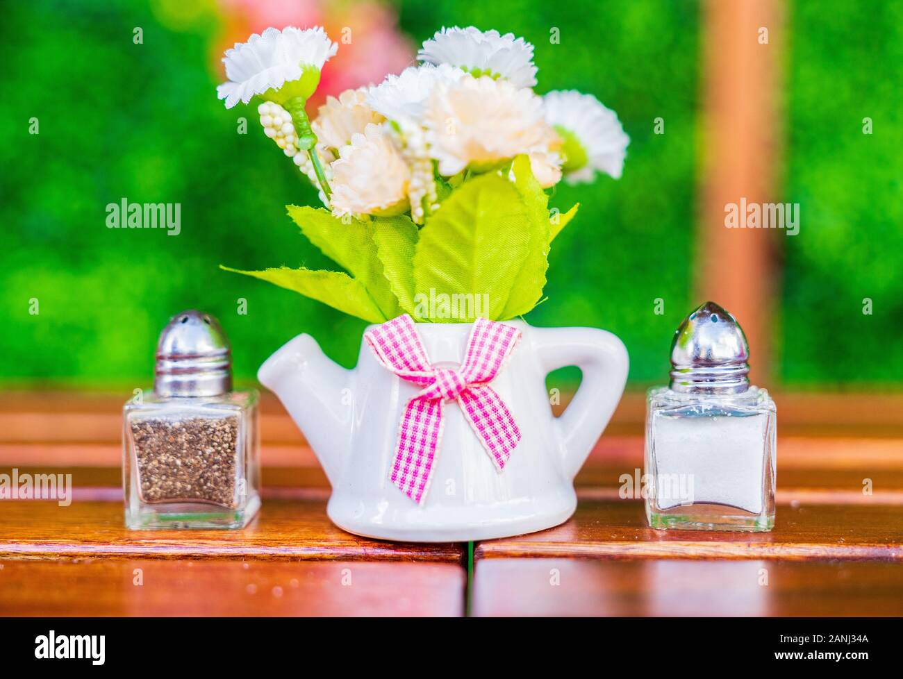 Blumenarrangement mit Salz- und Pfefferschüttlern und grünem Hintergrund. Stockfoto