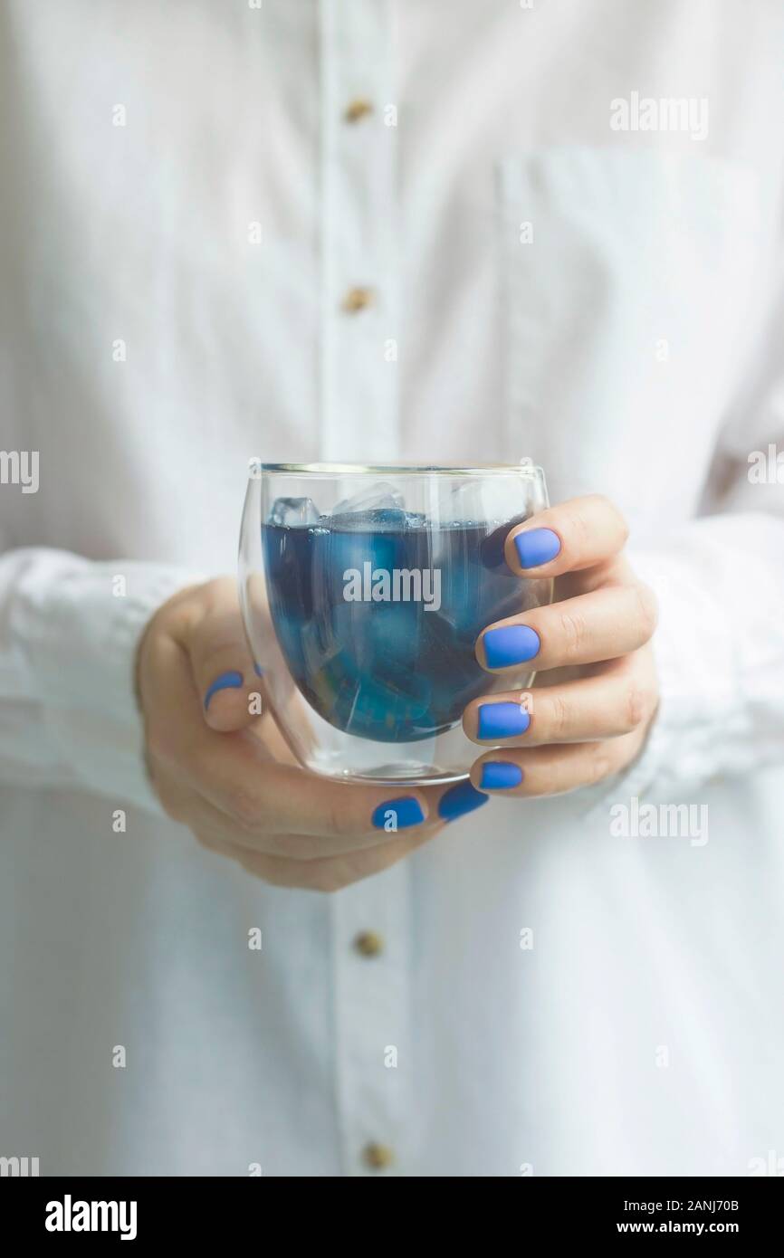 Blau Matcha kaltes Getränk mit Eis in ein Becherglas in die Hände einer Frau mit blauen Maniküre. Farbe des Jahres Trend 2020 Stockfoto