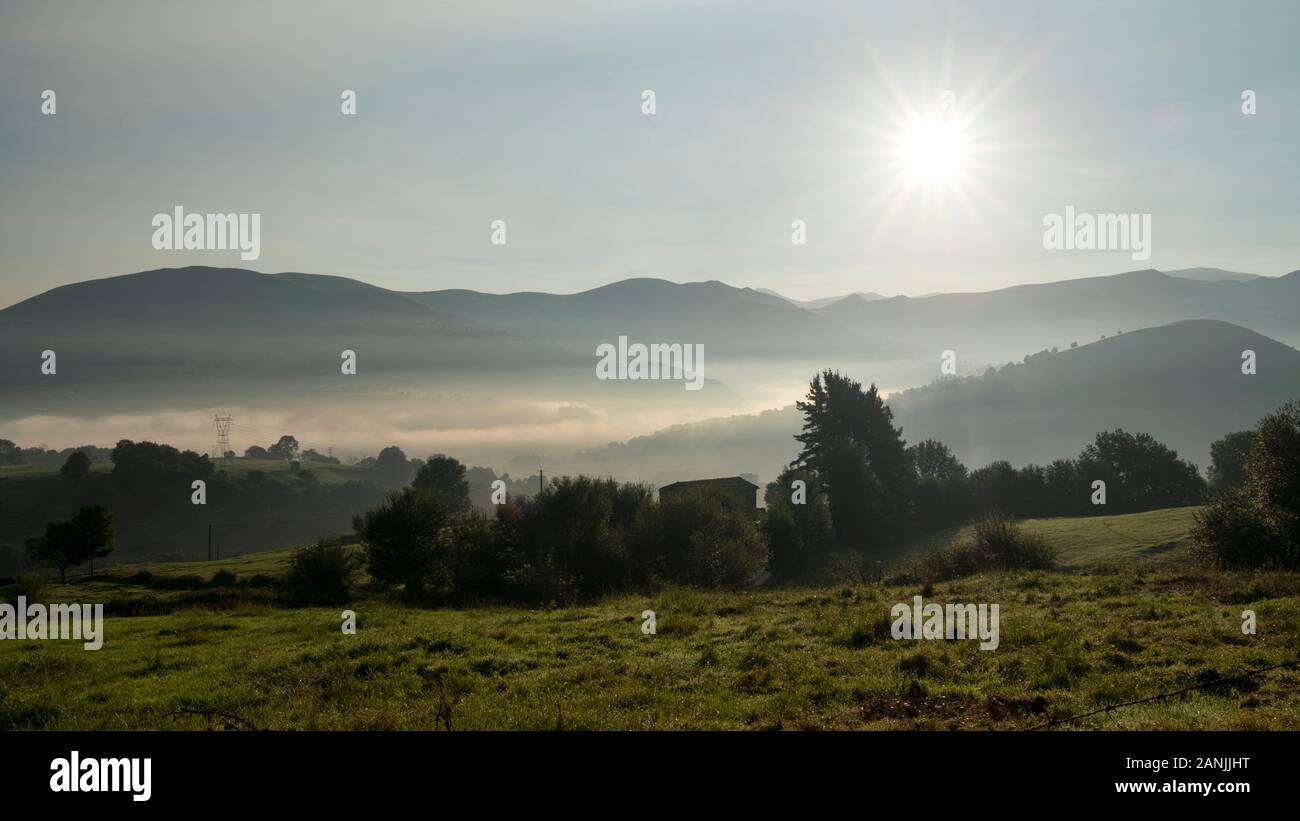 Almen und Hügel der Landschaft des Valle de Carriedo-Tals bei Sonnenaufgang mit Nebel bedeckt (Tezanos, Villacarriedo, Valles Pasiegos, Kantabrien, Spanien) Stockfoto