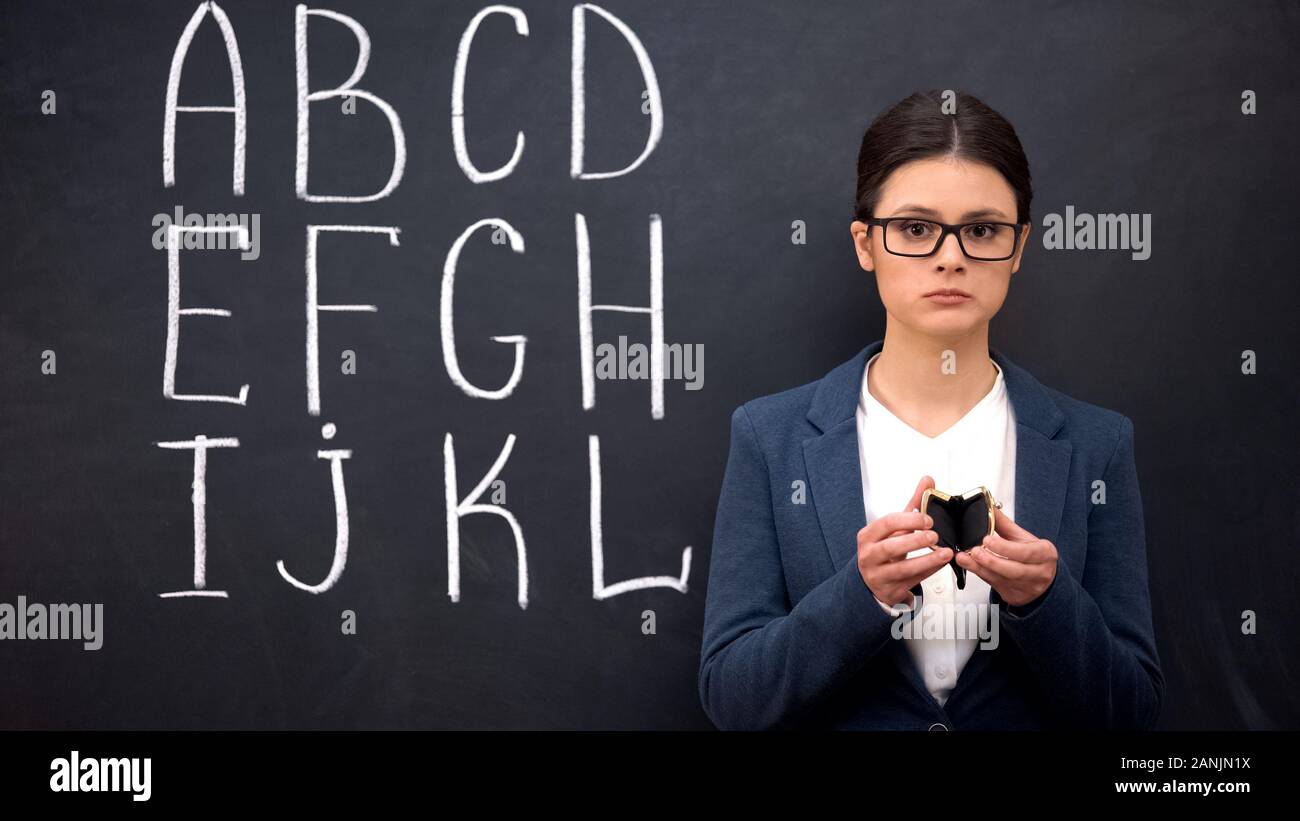 Frustrierte Lehrer zeigen leere Mappe, schlechte Finanzierung, Alphabet auf der Tafel Stockfoto