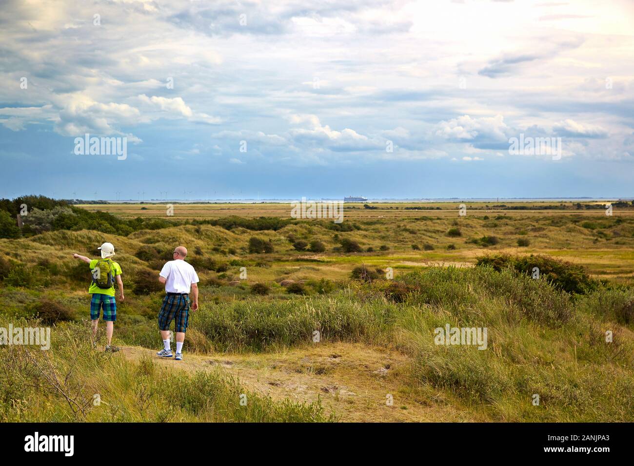 Zwei Personen, die die Umgebung vom Aussichtspunkt Old Dune auf der Insel Borkum aus mit Fährschiff und Windkraftanlagen im Hintergrund erkunden Stockfoto