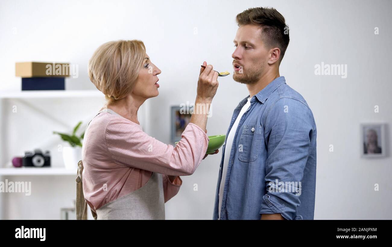 Mutter versuchen, erwachsener Sohn mit Löffel, überbehütung Problem zu füttern, Protest Stockfoto