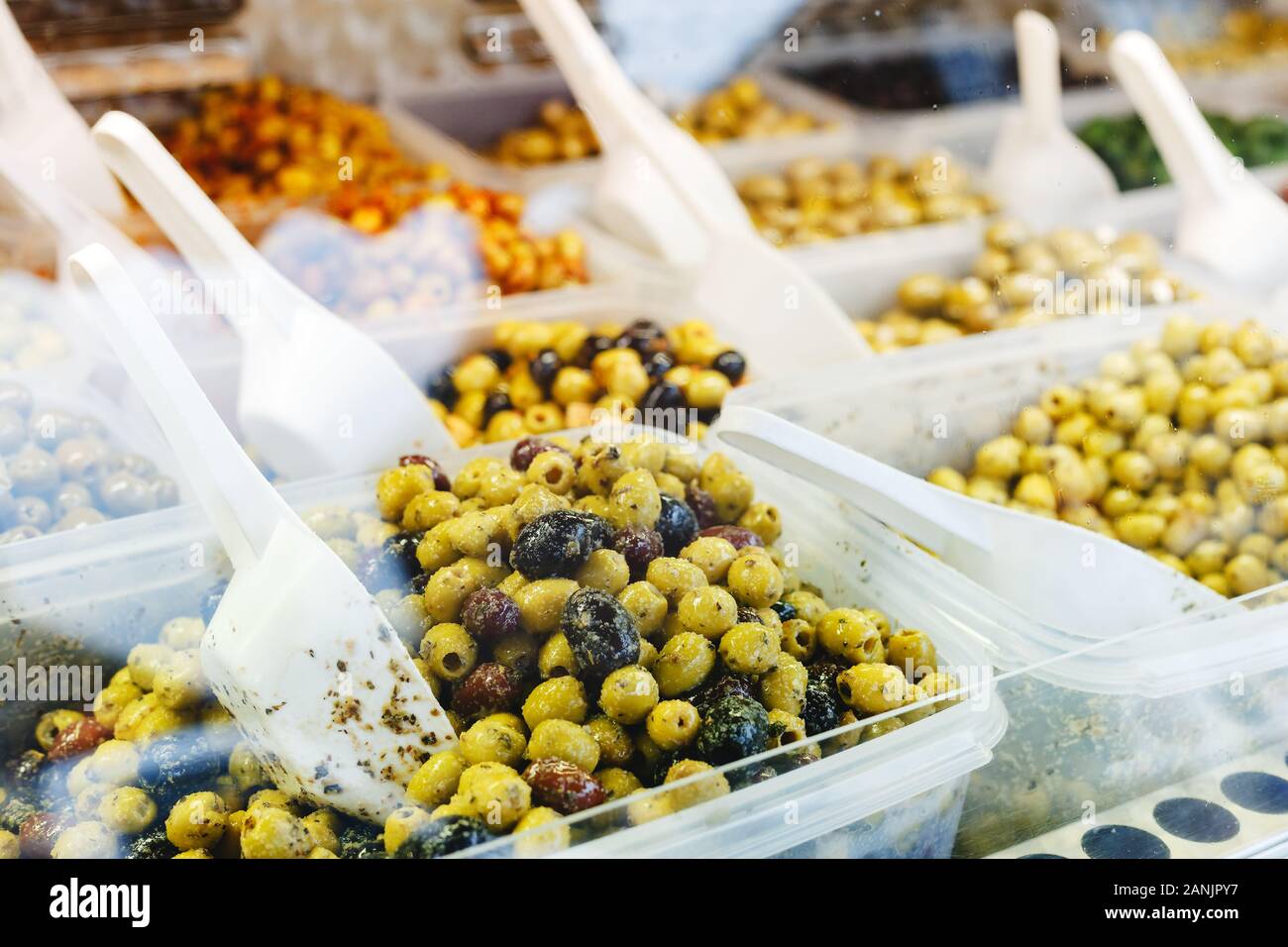 Verschiedene Arten von Oliven im Markt. Mix grün, schwarze Oliven mit Knoblauch, Pesto, Kräuter auf einen Zähler mit einem Messlöffel zum Verkauf. Foto traditio Stockfoto