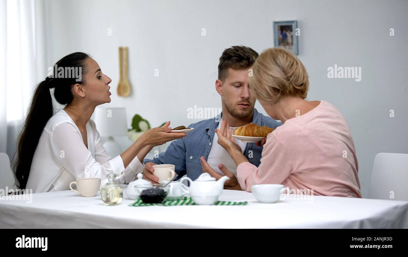 Frau und Schwiegermutter kämpfen für bemannt Aufmerksamkeit, schlägt Croissants und Kuchen Stockfoto
