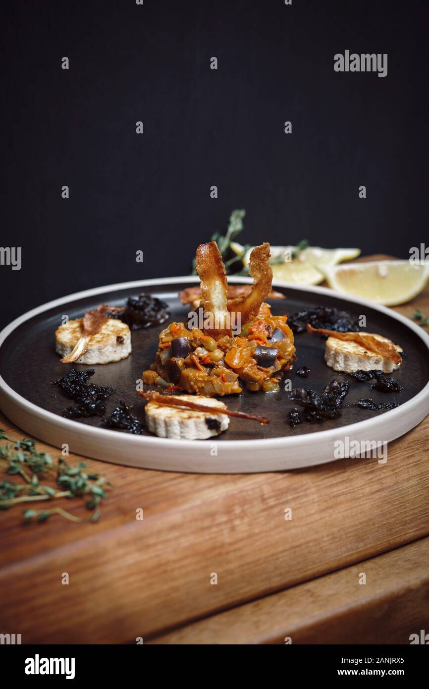 Veganer Hauptgang von Aubergine oder Aubergine & Tomaten-Ragu mit Tofu, Parsnip & Seetang auf einem Teller auf schwarzem Grund serviert. Draufsicht. Stockfoto
