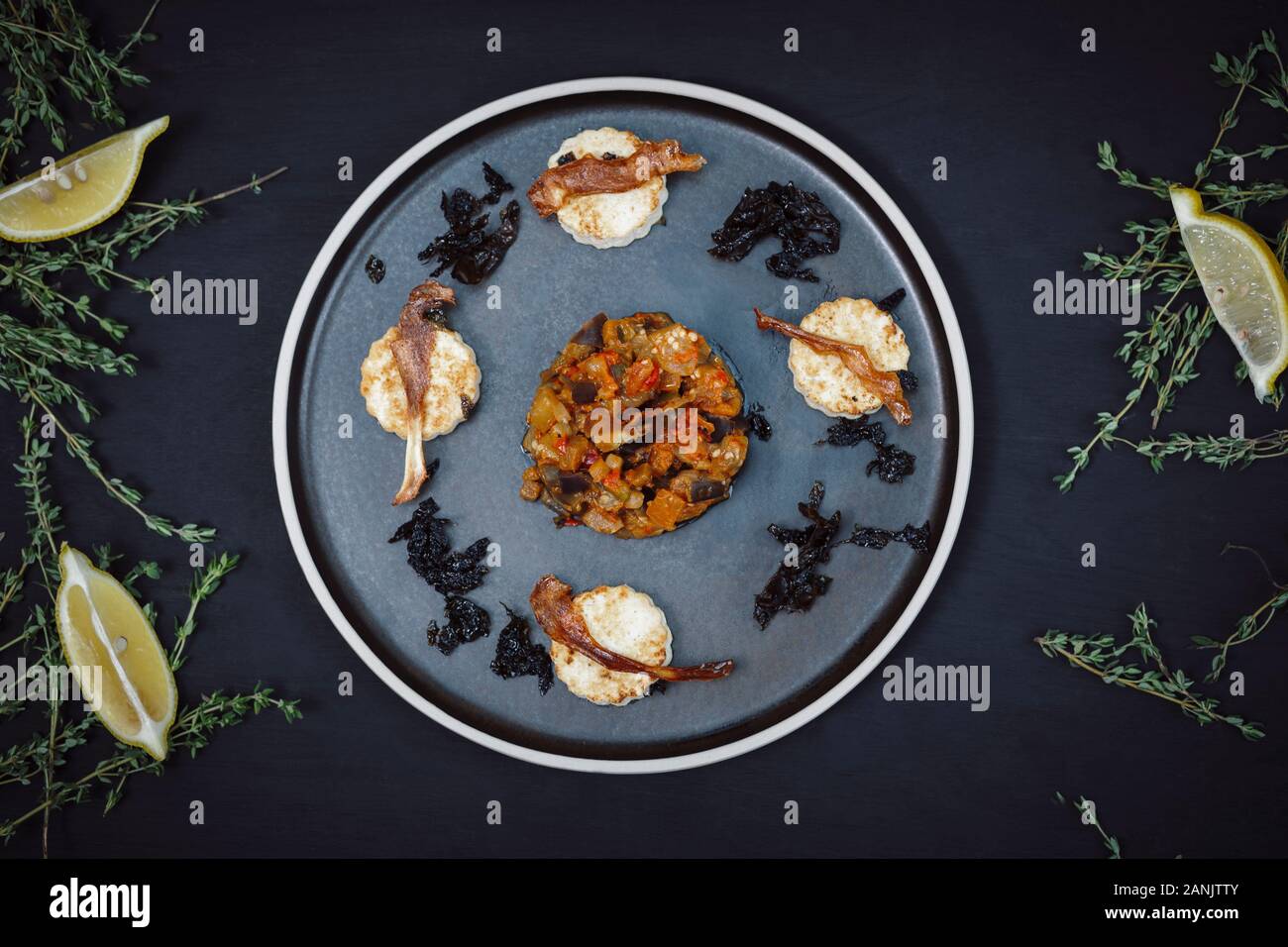 Veganer Hauptgang von Aubergine oder Aubergine & Tomaten-Ragu mit Tofu, Parsnip & Seetang auf einem Teller auf schwarzem Grund serviert. Draufsicht. Flaches Lay Stockfoto