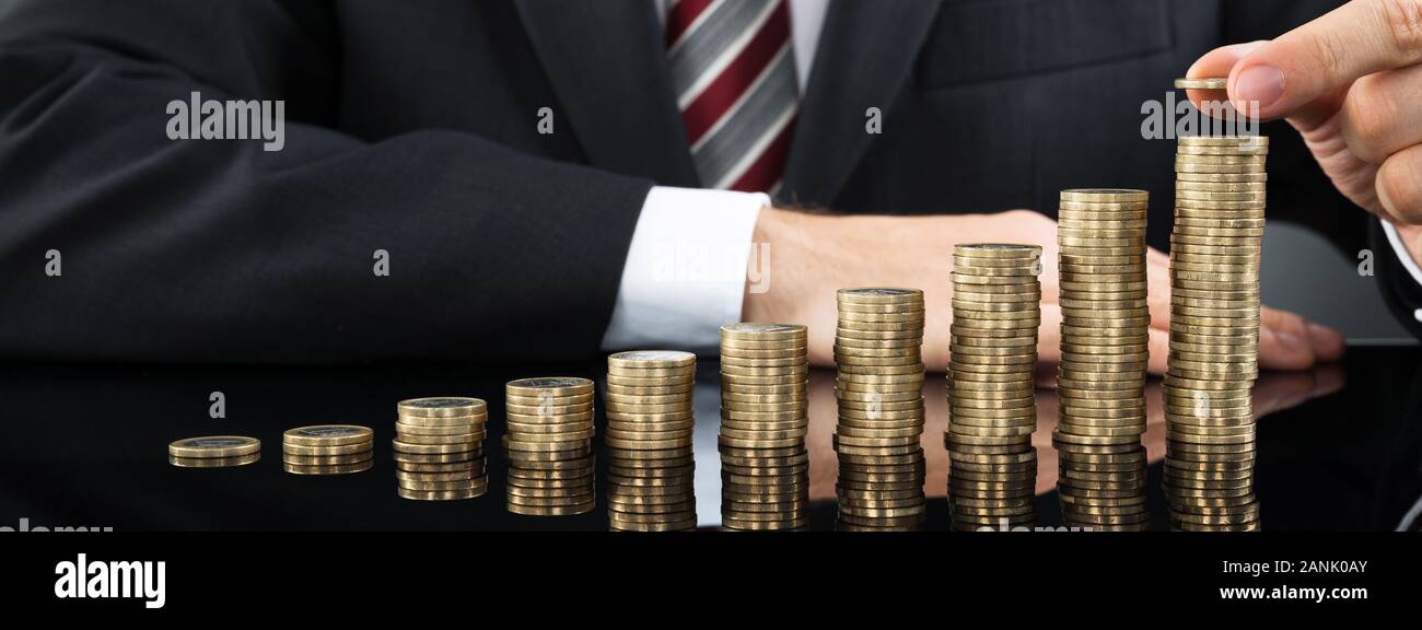 Nahaufnahme der Geschäftsmann Inverkehrbringen Münze über Stapel von Münzen am Schreibtisch Stockfoto