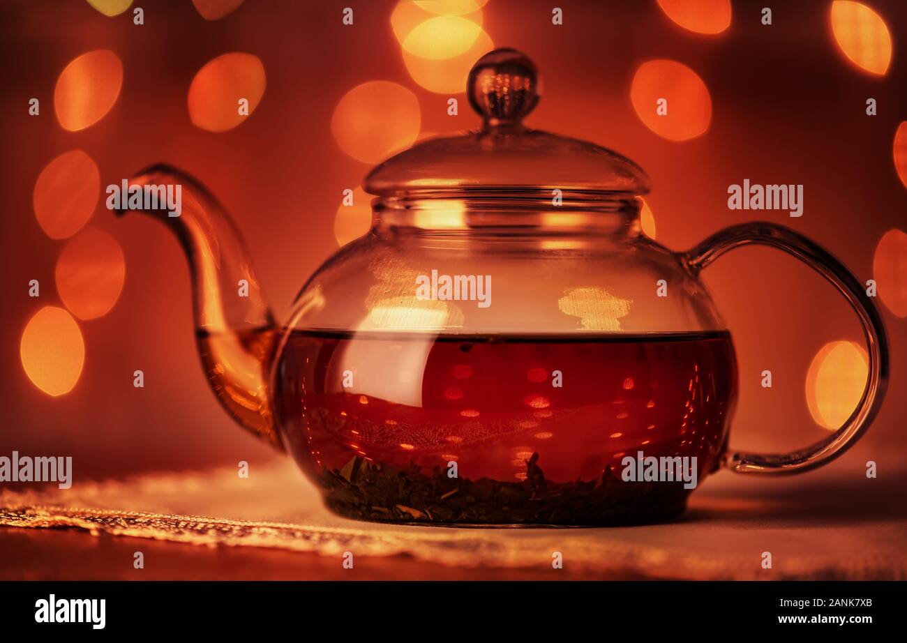 Teekanne aus Glas auf dunklem Hintergrund mit goldenen Bokeh leuchtet Stockfoto
