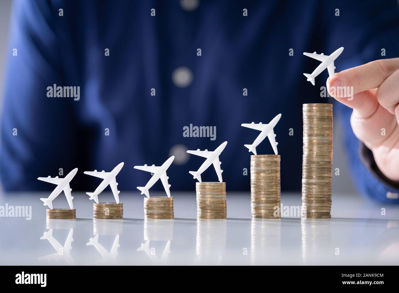 Nahaufnahme einer menschlichen Hand kleinen Flugzeug auf zunehmende Gestapelte Münzen über Schreibtisch Stockfoto