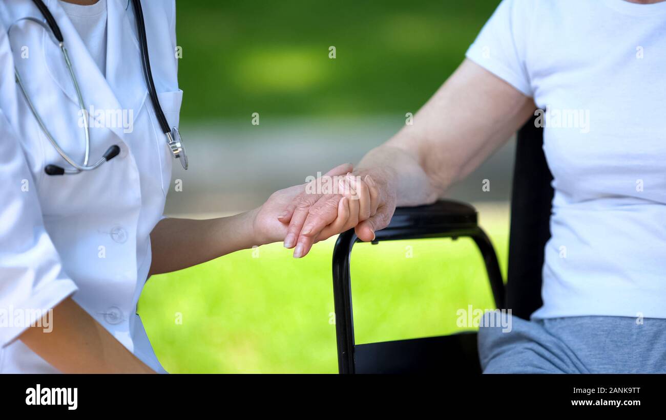 Therapeuten die Hand von Behinderten ältere Frau im Rollstuhl, im Freien Stockfoto