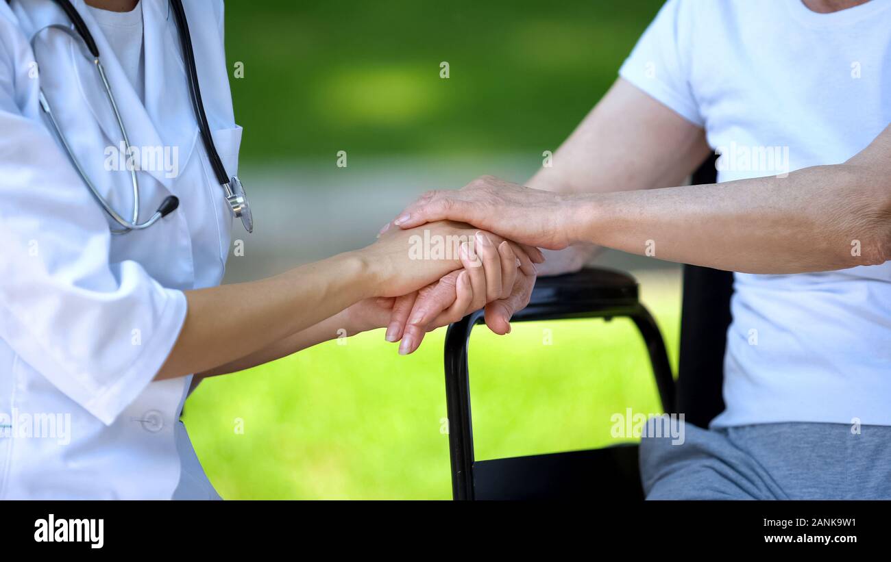 Weibliche Krankenschwester die Hand der behinderten Frau im Rollstuhl, fürsorgliches Personal Stockfoto