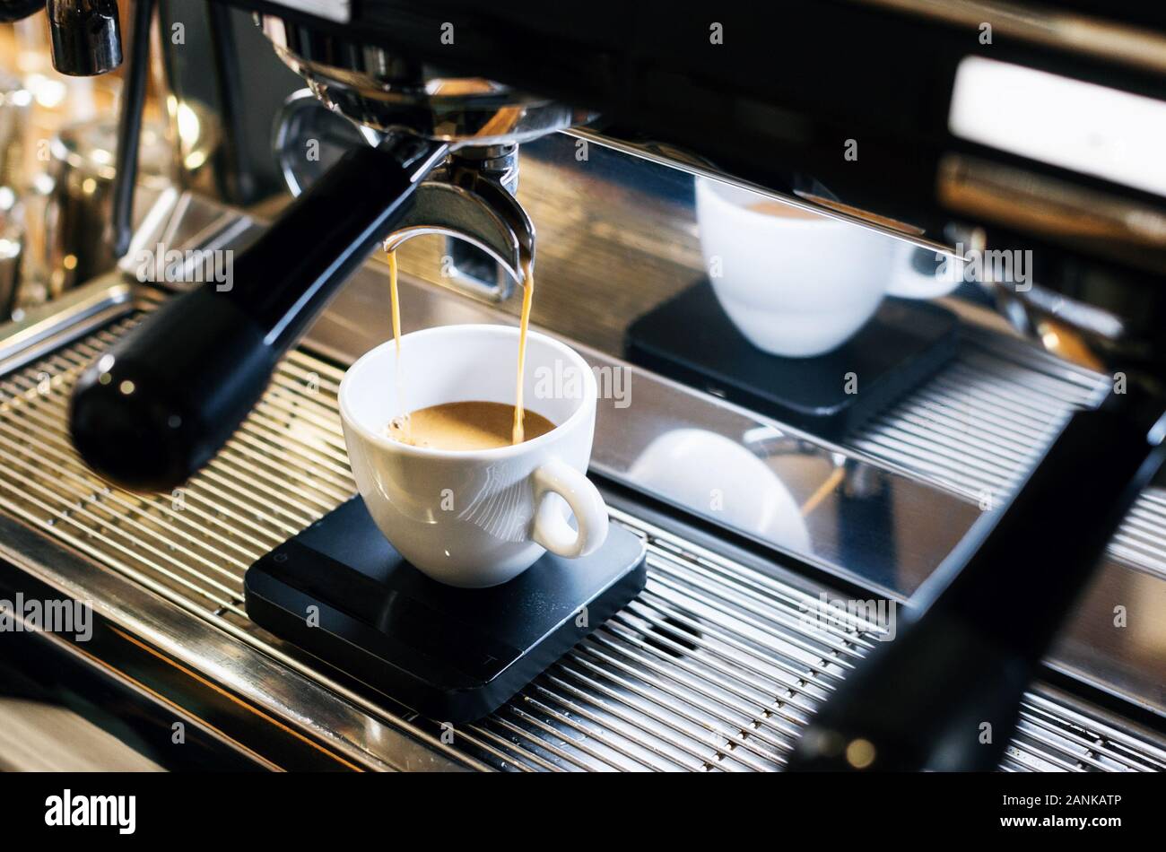 Professionelle Espressomaschine gießen frischen Kaffee in die weiße Keramiktasse mit Reflexion auf Hintergrund Stockfoto