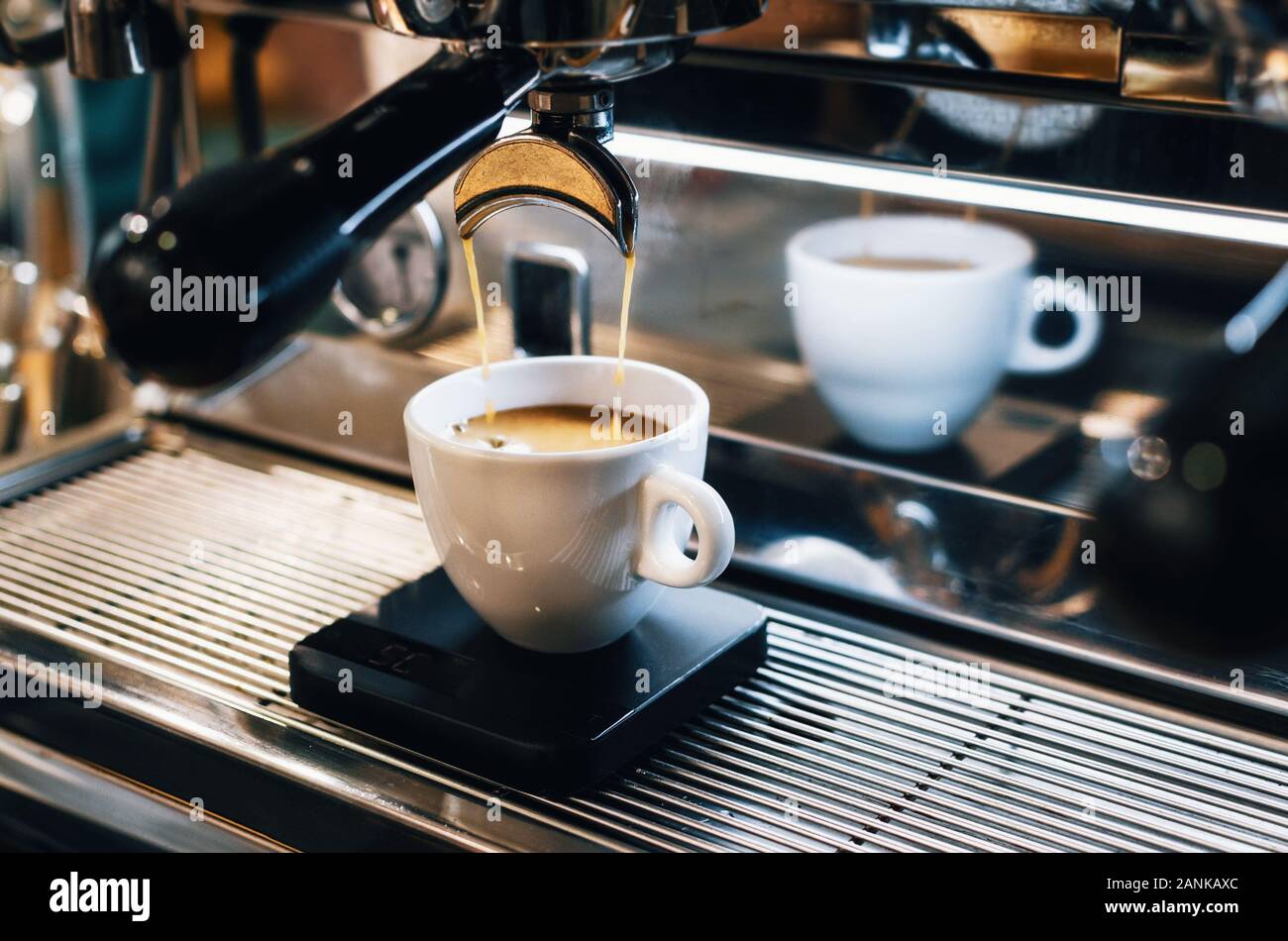 Professionelle Espressomaschine gießen frischen Kaffee in die weiße Keramiktasse mit Reflexion auf Hintergrund Stockfoto