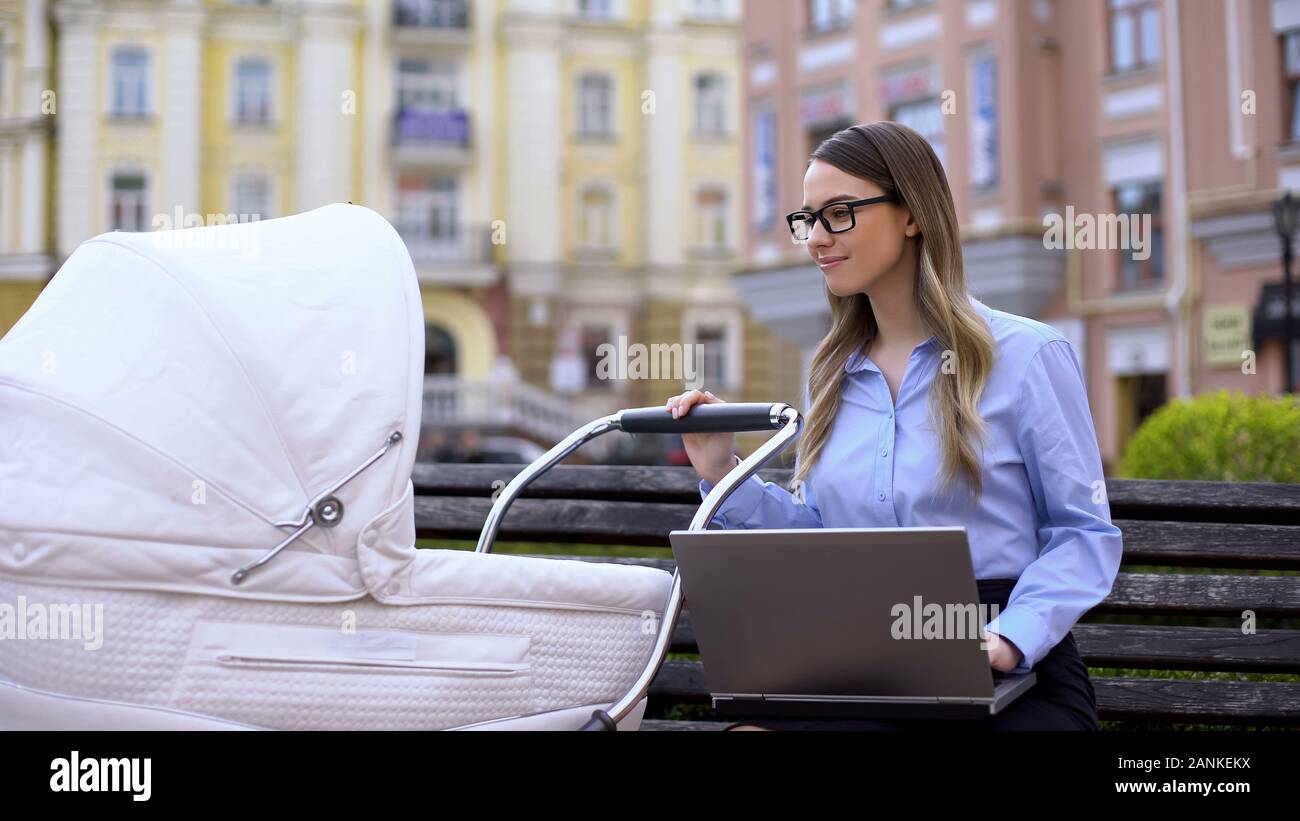 Gerne Mama mit Laptop schwingen Neugeborenen im Schlitten, Familie und Karriere Stockfoto