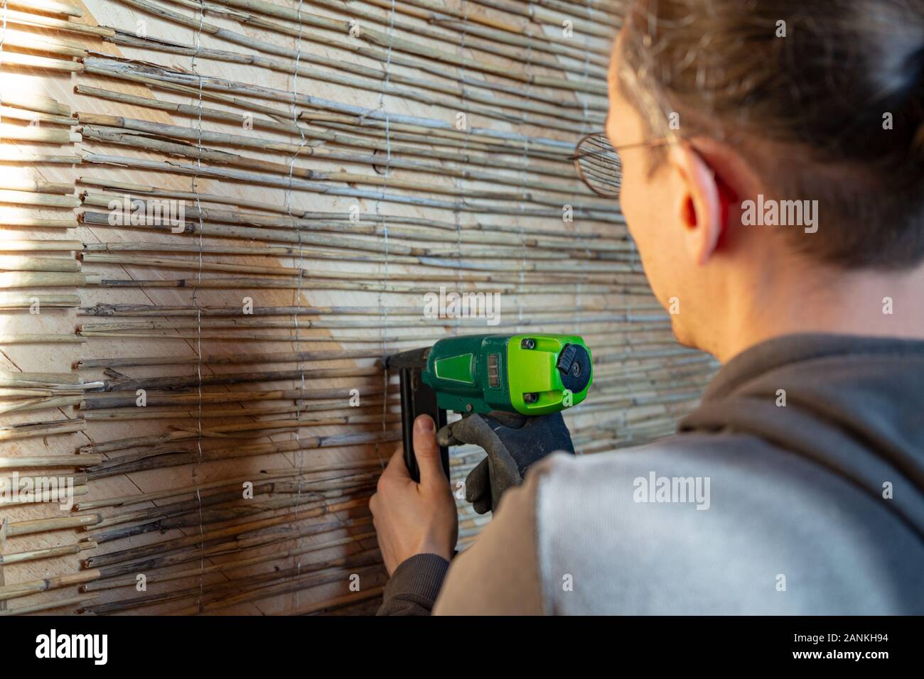 Der Mensch ist das Fixieren reed Mats auf einer Holzwand für plastring die Wände mit Lehm und Sand - Begriff der Moderne und ökologische Architektur vorzubereiten Stockfoto