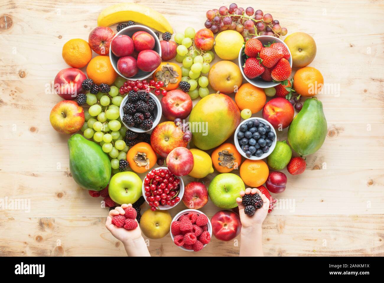 Die Hand des Kindes, die Herzen von gesunden rainbow Früchten, Pflaumen Erdbeeren Himbeeren Orangen, Äpfel, Kiwis, Weintrauben, Heidelbeeren mango Papaya auf Holztisch, Ansicht von oben, Kopieren, selektiven Fokus Stockfoto