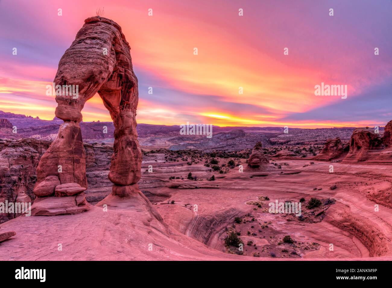 Zarte Arch am Rande einer kreisförmigen Kante gegen eine lebendige Sonnenuntergang Himmel im Arches National Park, Moab, Utah. Stockfoto