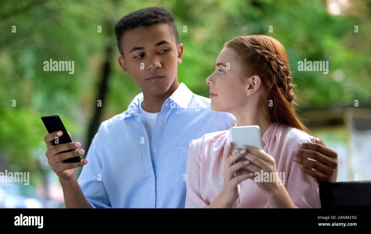 Mixed-race teen Paar sich einander Plaudern auf Smartphone in Park Stockfoto